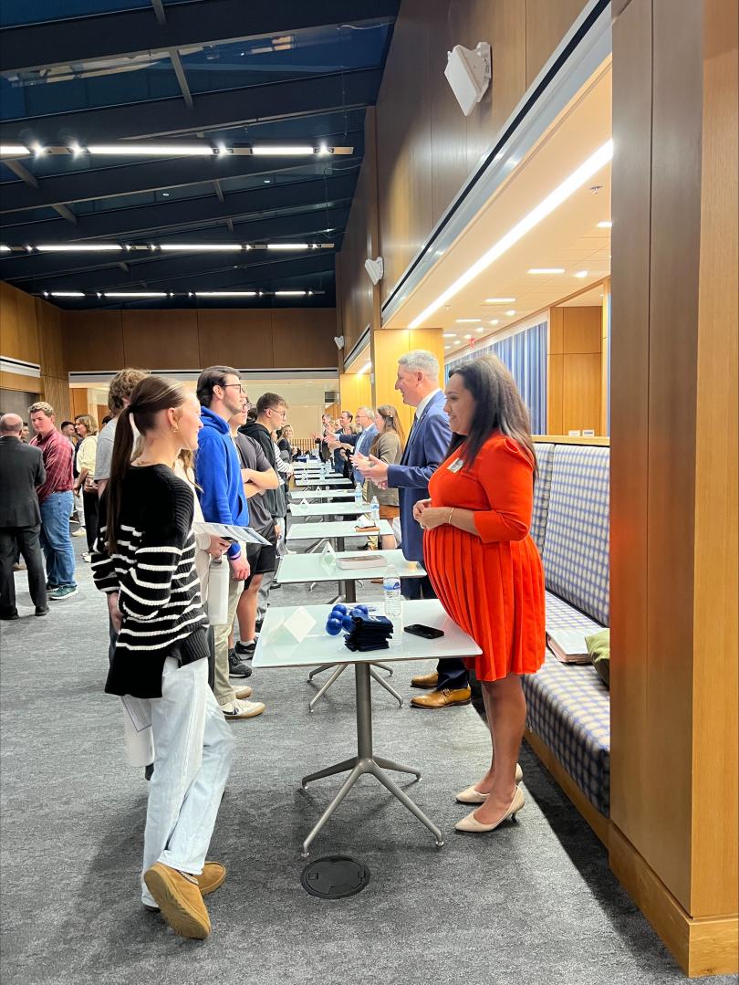 Professonally-dressed people gather across small tables, engaged in conversation.
